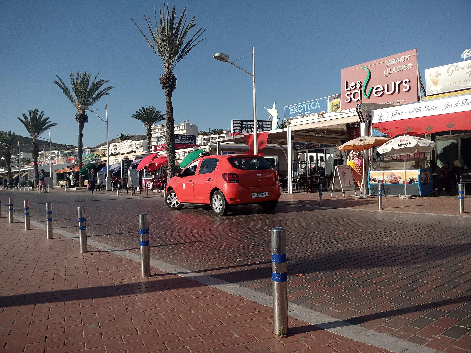 Un petit taxi rouge dans une rue marocaine bordée de palmiers